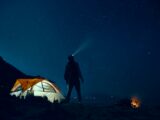 man standing beside camping tent wearing headlamp during nighttime